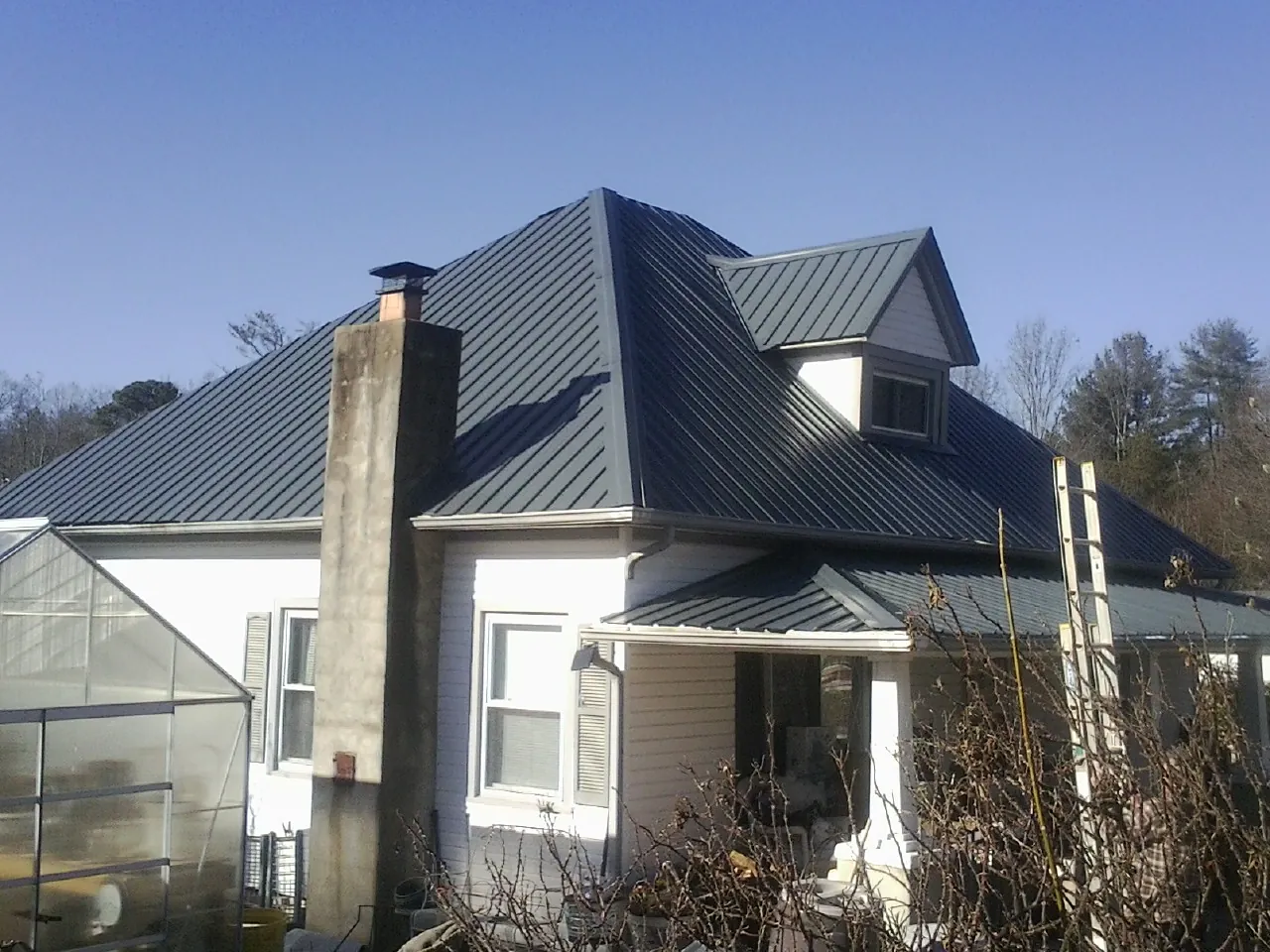 Dark blue standing seam metal roof on a white farmhouse with dormer — Slate & Tile Roof Repair by Roofing Brothers in Irvington