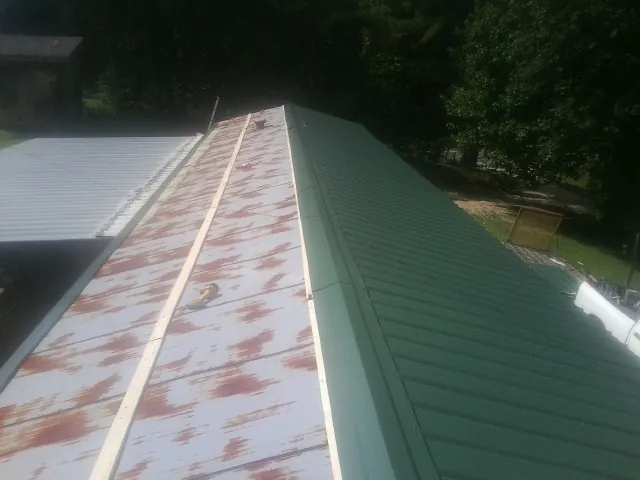 Old rusted panels beside newly installed green metal roofing — Wind Damage Roof Repair by Roofing Brothers in Irvington